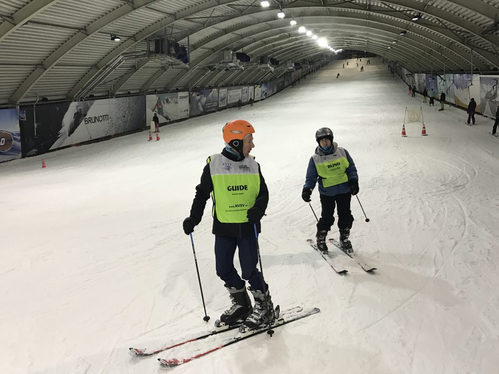 Twee personen met gele hesjes die skiën in een skihal 